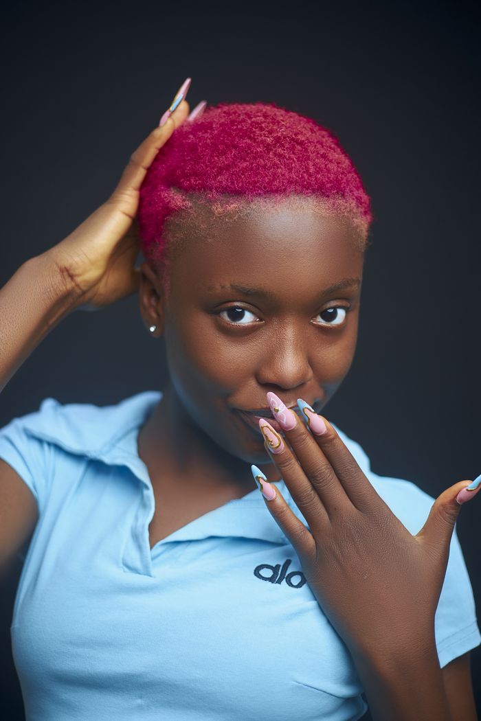 services-01 Close-up portrait of a woman with bold pink hair and artistic nails in a playful pose.